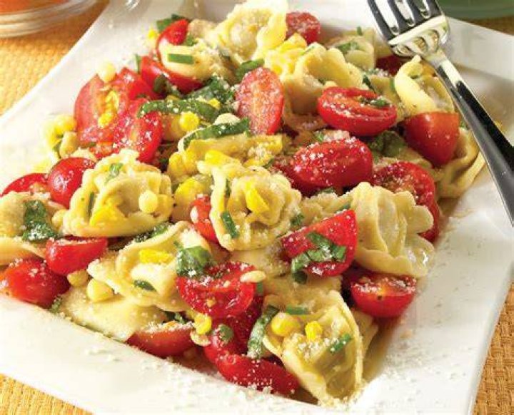 Bowl with tortellini, corn, tomatoes, zucchini, basil.