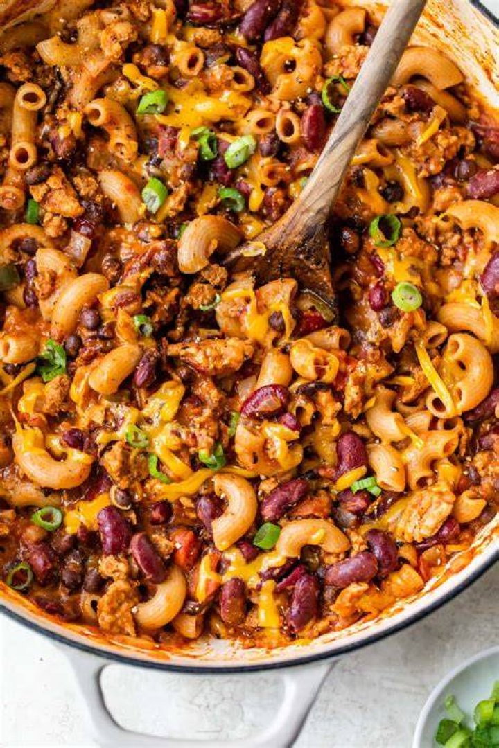 Chili mac in a red bowl topped with grated cheese.